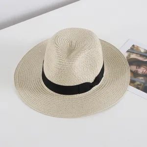 Vista detallada de un elegante sombrero de paja beige con cinta negra sobre una superficie limpia.