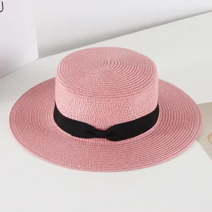 Pink straw hat with a black ribbon bow, perfect for summer beach vacations, sun protection.