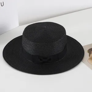 Detail view of a stylish black flat top straw hat with ribbon bow for summer beach travel.