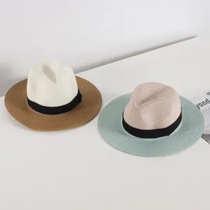 Detailed view of women straw fedoras with black bows, summer beach sun hats on clean white surface.