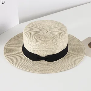 Detail view of a Korean style flat-top straw hat with a black bow ribbon for summer sun protection.