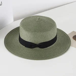 Green straw hat detail showing the fine woven texture and elegant black ribbon bow decoration.