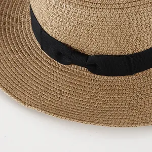 Close-up view of summer straw hat woven texture featuring elegant black ribbon bow detail.