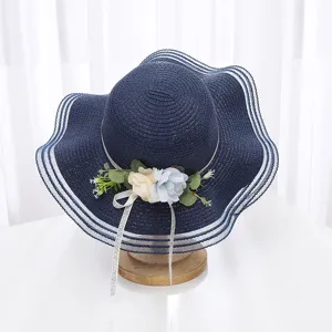 Détail de chapeau de paille bleu marine, avec décoration florale et large bord en filet ondulé.