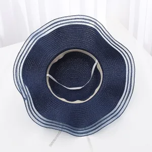 Détail de chapeau de paille d'été bleu marine, bord en tulle blanc élégant et élastique intérieur.