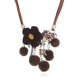 Close up detail of the bohemian woven flower and fluffy pom-pom pendant on the brown cord.