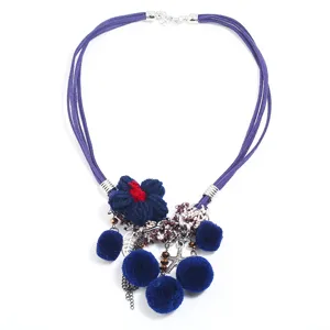 Detailed view of bohemian multi-strand purple cord necklace with knitted flower and blue pom-poms.