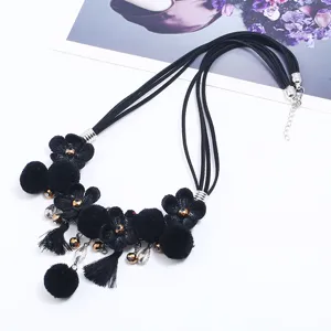 Close-up detail of black layered fabric flower necklace with pompoms and tassels.