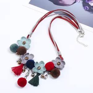 Detail view of multi-strand suede necklace featuring fabric flowers, pompoms, and tassels.