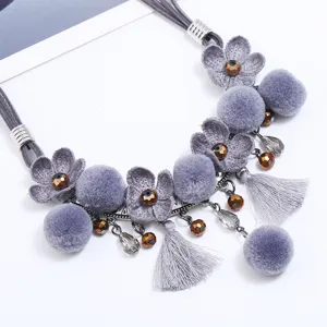 Detailed close-up view of a grey fabric flower and fluffy pom-pom tassel necklace.
