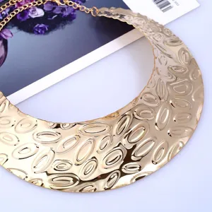 Close-up of an exaggerated gold metallic collar necklace featuring a textured embossed oval pattern.