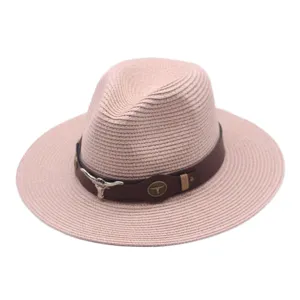 Gros plan d'un élégant chapeau de paille rose avec bande en cuir et crâne de taureau en métal.