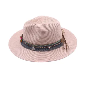 Sombrero fedora de paja rosa con banda tejida colorida, borlas y lazo de cuero en el lateral.