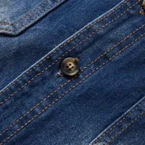Detailed view of mens casual denim shirt featuring contrast stitching and button closure.