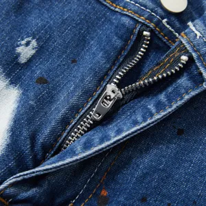 Primo piano di pantaloncini in denim blu da uomo con schizzi di vernice e zip metallica.
