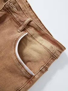 Dettaglio jeans da uomo, tessuto lavato marrone con cuciture bianche e tasca classica.