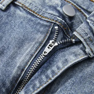 Primo piano dettaglio di patta con zip e bottone in metallo di pantaloncini denim uomo lavati.