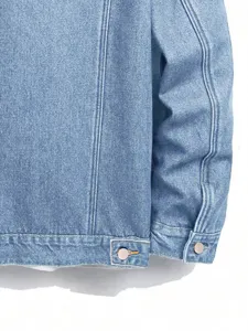 Primer plano de manga y dobladillo de chaqueta vaquera con botón metálico y costuras.