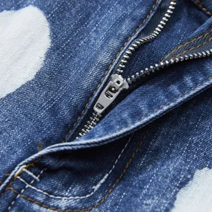 Close-up detail of men's stretch denim shorts zipper, splash ink design, blue wash fabric.