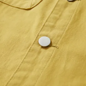Primer plano de la tapeta de camisa vaquera amarilla con botón a presión de metal y costuras.