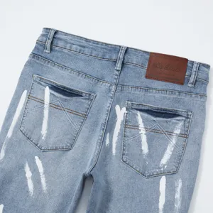 Primo piano dettagli pantaloncini denim stretch uomo con macchie di inchiostro e toppa in pelle.
