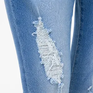 Close-up detail of women's distressed ripped denim jeans knee section wash fabric texture.