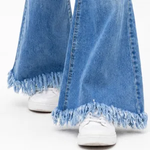 Detailed shot of women's blue denim flare jeans featuring distressed tassel hems and white sneakers.