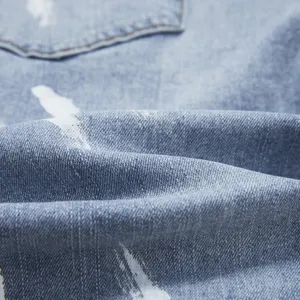 Primo piano dettagliato di tessuto denim azzurro con effetto schizzi di vernice bianca.