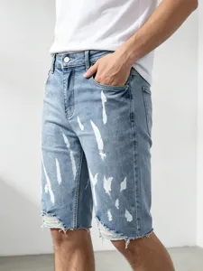 Short in denim elasticizzato da uomo con schizzi di bianco e orlo sfrangiato di moda.