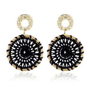 Detailed shot of bohemian style metal and woven drop earrings featuring a textured gold disc.