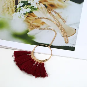 Lange Goldkette mit einem schicken runden Metallring und roten Quasten als anhaenger.