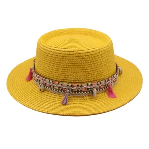 Detailansicht des gelben Strohhutes mit buntem geflochtenem Band, rosa Quasten und Muschelanhängern.