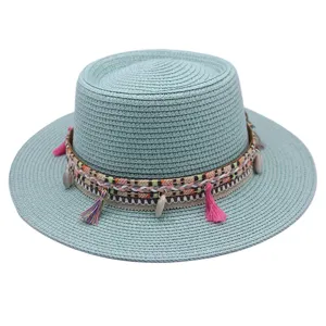 Detailansicht eines mintgrünen flachen Strohhutes mit Ethnoband und pinken Quasten.