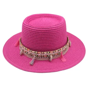 Rosa flacher Strohhut mit ethnischem Webband, Quasten und Muscheln fuer den Sommerstrandurlaub.