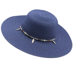 Primer plano detallado del sombrero de paja azul con cuentas de madera y dijes de plumas.