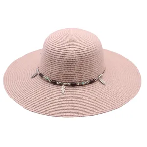 Detalle de sombrero de paja rosa, ala ancha de playa con cuentas y plumas elegantes.