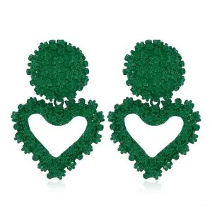 Dettaglio orecchini a cuore goffrati floreali verdi, gioielli pendenti in metallo.