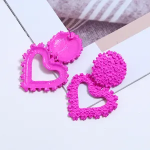 Dettaglio degli orecchini pendenti a cuore rosa vivo con motivi floreali metallici.