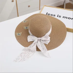 Detail of summer straw sun hat with wide brim, pink ribbon bow and cute butterfly embroidery.