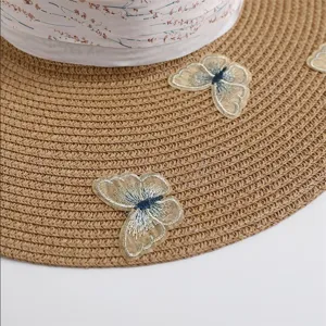 Close-up detail of summer straw sun hat featuring exquisite embroidered butterflies and floral ribbon.