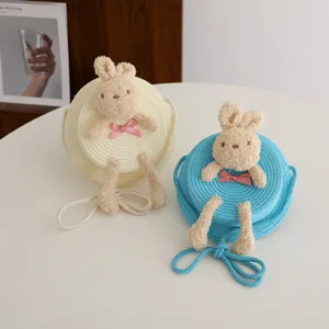 Dettaglio borsa a tracolla in paglia per bambini con coniglietto di peluche e fiocco.