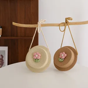 Dettaglio borsa a tracolla di paglia per bambini, borsa rotonda tessuta con fiore rosa.
