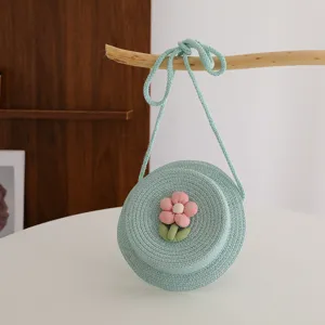 Vista dettagliata di una graziosa borsa rotonda in paglia verde menta con fiore rosa.