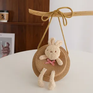 Dettaglio della borsa rotonda in paglia carina con coniglietto peluche soffice e fiocco rosa.