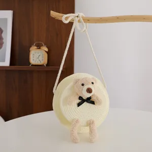 Dettaglio della borsa a tracolla rotonda in paglia con orsetto di peluche e fiocco.