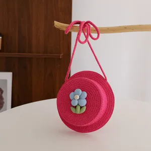 Borsa a tracolla rotonda in paglia intrecciata rosa per bambini con fiore blu per spiaggia.