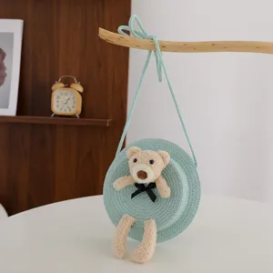Dettaglio di borsetta in paglia rotonda con orsetto di peluche e fiocco nero per ragazze.