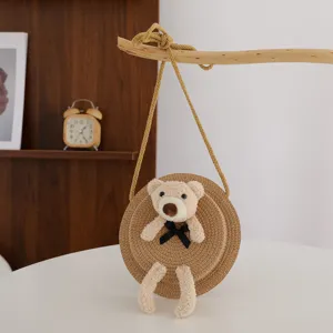 Dettaglio borsa a tracolla in paglia con orsetto di peluche, perfetta per la spiaggia estiva.