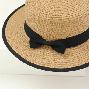 Vue détaillée d'un chapeau de paille d'été avec calotte plate, nœud et bord noirs.