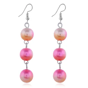Nahaufnahme von langen Ohrringen mit drei Perlen in sanftem Farbverlauf von Rosa zu Orange.